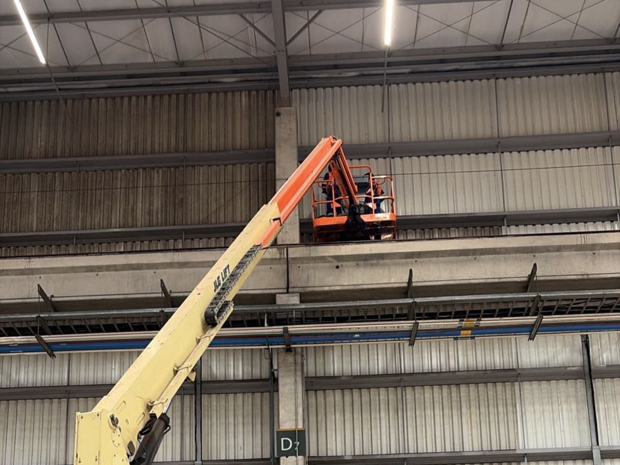 Equipe em plataforma elevatória limpando parede interna de galpão industrial